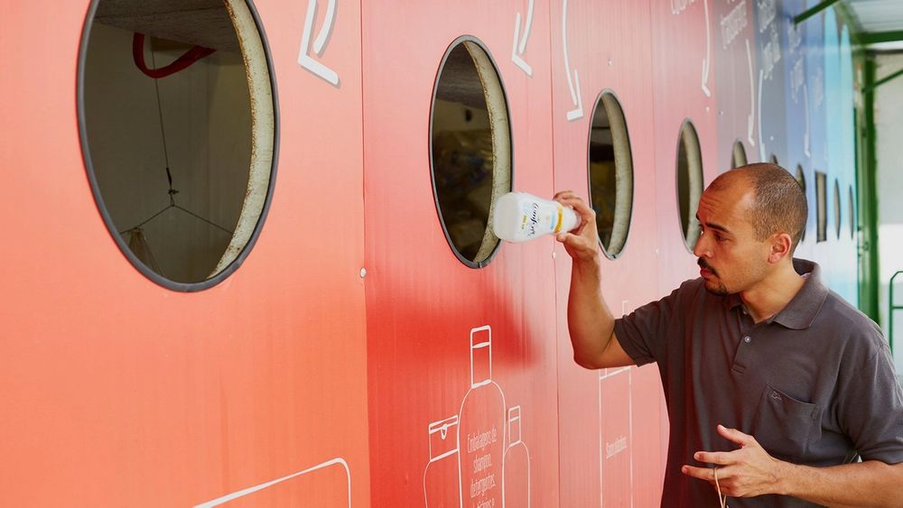 Man deponeert een plastic fles in een grote kleurrijke recyclewand.